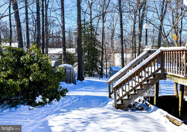 yard covered in snow featuring a wooden deck and a storage unit