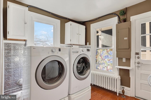 laundry area featuring washing machine and clothes dryer, electric panel, cabinets, radiator, and wood-type flooring