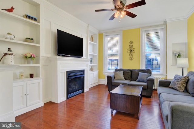 living room with crown molding, radiator, ceiling fan, dark wood-type flooring, and built in features