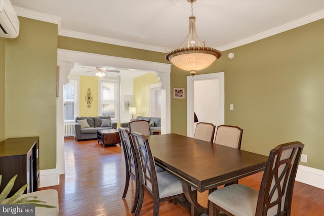 dining space with an AC wall unit, ceiling fan, hardwood / wood-style flooring, ornamental molding, and radiator heating unit