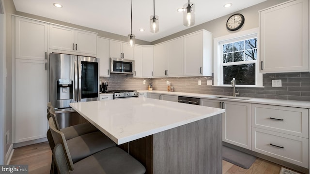 kitchen featuring sink, hanging light fixtures, a kitchen island, white cabinets, and appliances with stainless steel finishes