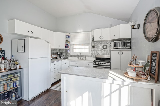 kitchen featuring lofted ceiling, backsplash, white cabinetry, appliances with stainless steel finishes, and dark hardwood / wood-style flooring