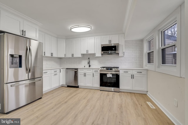 kitchen featuring appliances with stainless steel finishes, light hardwood / wood-style floors, tasteful backsplash, and white cabinetry