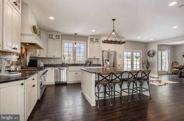 kitchen with stainless steel appliances, decorative light fixtures, white cabinetry, dark hardwood / wood-style floors, and a kitchen island