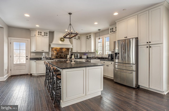 kitchen featuring stainless steel fridge, custom exhaust hood, white cabinets, a center island, and hanging light fixtures