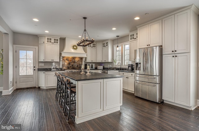 kitchen with premium range hood, white cabinets, hanging light fixtures, a kitchen island, and stainless steel fridge with ice dispenser