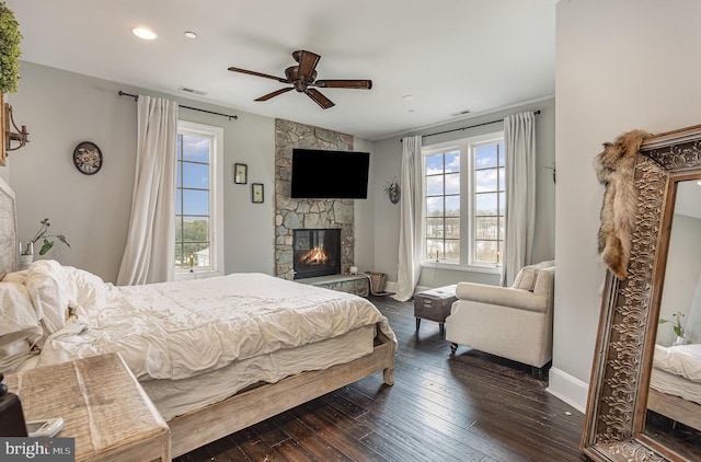 bedroom with ceiling fan, dark hardwood / wood-style flooring, and a stone fireplace