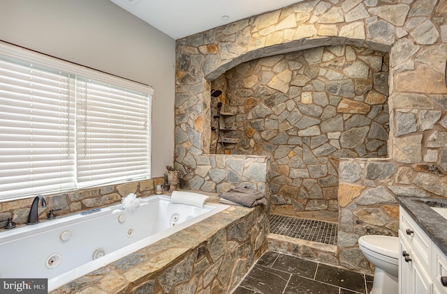 bathroom featuring vanity, a relaxing tiled tub, and toilet