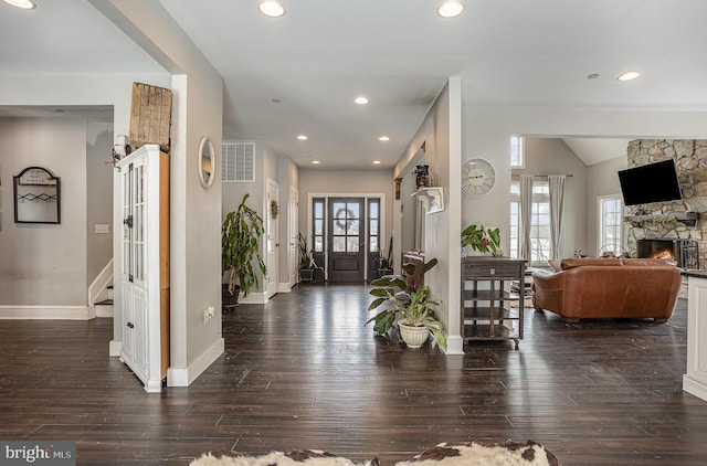 foyer entrance with dark hardwood / wood-style flooring, a stone fireplace, and vaulted ceiling