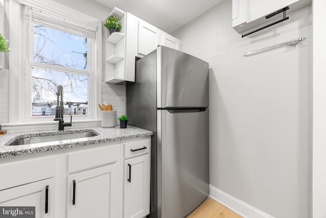 kitchen featuring light stone countertops, white cabinets, tasteful backsplash, and stainless steel fridge