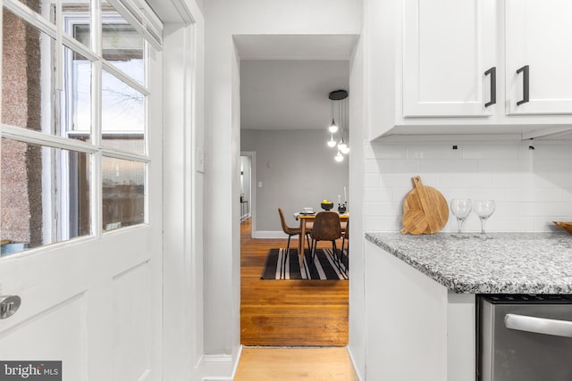 interior space featuring decorative backsplash, decorative light fixtures, light wood-type flooring, white cabinets, and light stone counters