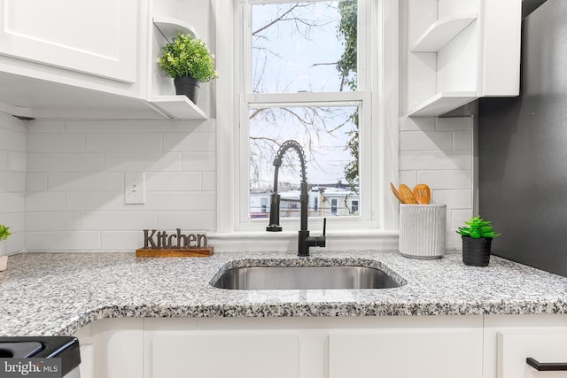 kitchen with tasteful backsplash, white cabinets, light stone countertops, and sink