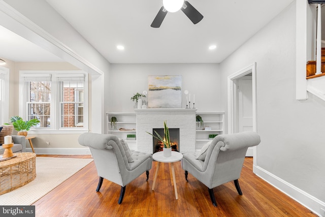 living area featuring ceiling fan, a fireplace, and hardwood / wood-style floors