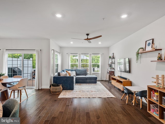 living room with a wealth of natural light, ceiling fan, and dark wood-type flooring