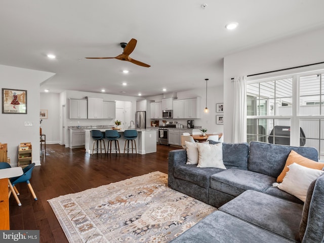 living room featuring ceiling fan, sink, and dark wood-type flooring