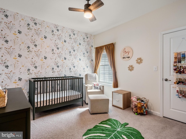 carpeted bedroom with a crib and ceiling fan