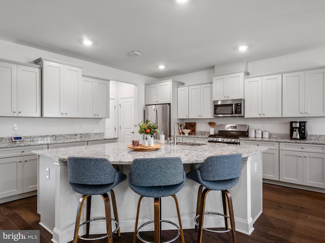 kitchen with sink, dark wood-type flooring, a center island with sink, white cabinets, and appliances with stainless steel finishes