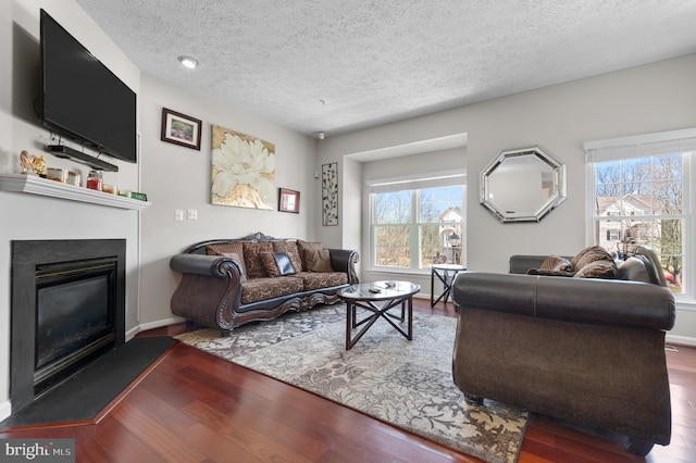 living area with a glass covered fireplace, wood finished floors, baseboards, and a textured ceiling