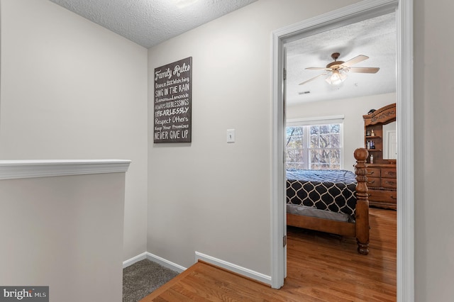 corridor with visible vents, a textured ceiling, baseboards, and wood finished floors