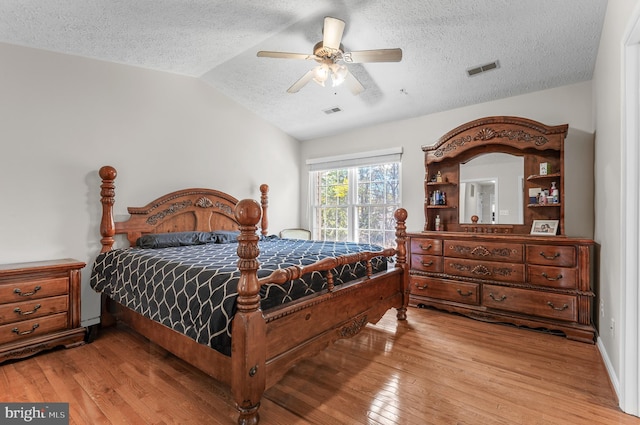 bedroom with light wood finished floors, visible vents, a textured ceiling, and lofted ceiling