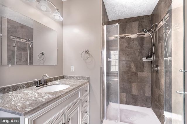 full bathroom with a textured ceiling, a stall shower, and vanity