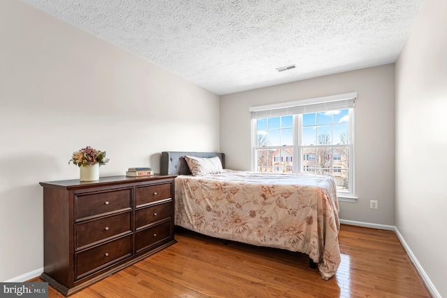 bedroom with a textured ceiling, wood finished floors, visible vents, and baseboards