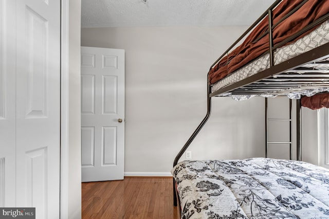 bedroom with baseboards, a textured ceiling, and wood finished floors