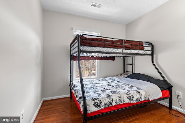 bedroom featuring visible vents, a textured ceiling, baseboards, and wood finished floors