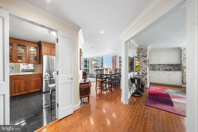 kitchen with light stone counters, ornamental molding, stainless steel fridge, and a wall of windows