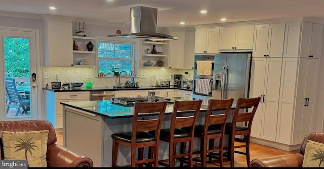 kitchen with appliances with stainless steel finishes, white cabinets, island exhaust hood, a breakfast bar, and sink