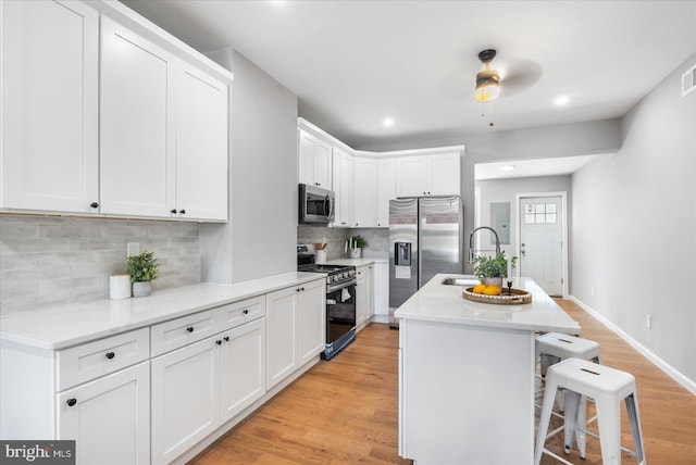 kitchen featuring stainless steel appliances, an island with sink, decorative backsplash, a breakfast bar, and white cabinets