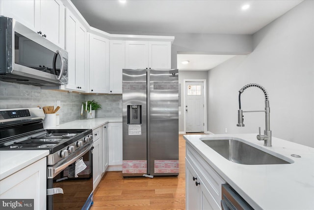 kitchen with white cabinetry, sink, backsplash, light hardwood / wood-style floors, and appliances with stainless steel finishes