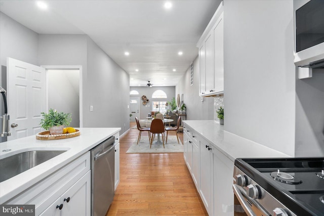 kitchen with white cabinetry, sink, ceiling fan, stainless steel dishwasher, and light hardwood / wood-style floors