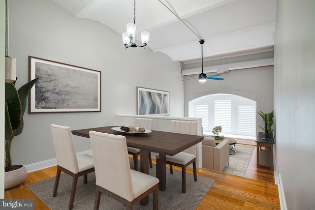 dining space with ceiling fan with notable chandelier, vaulted ceiling with beams, and light hardwood / wood-style flooring