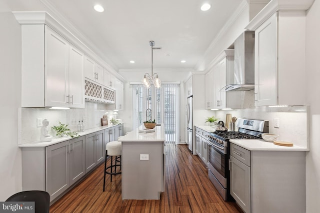 kitchen with a center island, wall chimney range hood, gray cabinets, a kitchen bar, and stainless steel appliances