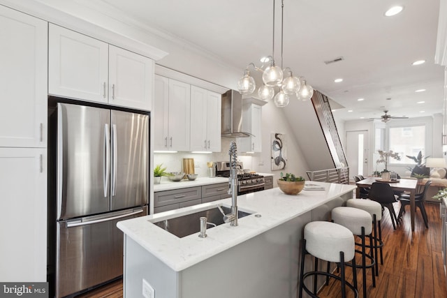 kitchen with white cabinetry, ceiling fan, stainless steel appliances, wall chimney range hood, and pendant lighting