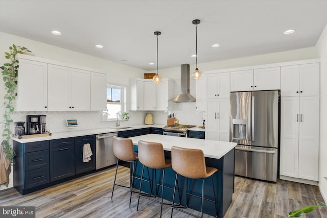 kitchen with a kitchen bar, light countertops, white cabinets, stainless steel appliances, and wall chimney exhaust hood