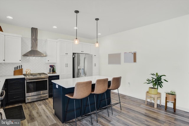 kitchen featuring stainless steel appliances, light countertops, wall chimney exhaust hood, tasteful backsplash, and a center island