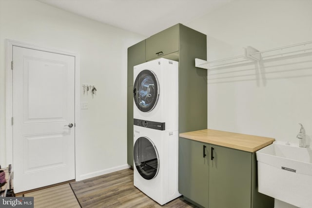 laundry room featuring a sink, wood finished floors, cabinet space, stacked washer / drying machine, and baseboards