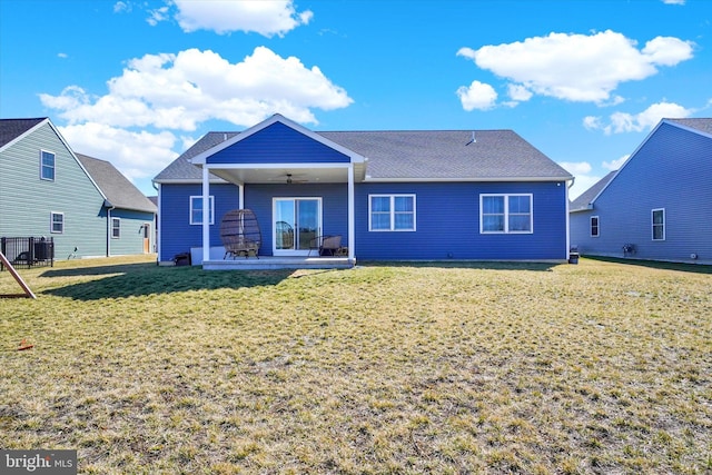 rear view of property featuring a ceiling fan, a lawn, and roof with shingles