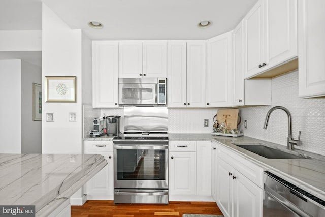 kitchen with white cabinets, appliances with stainless steel finishes, light stone countertops, and sink