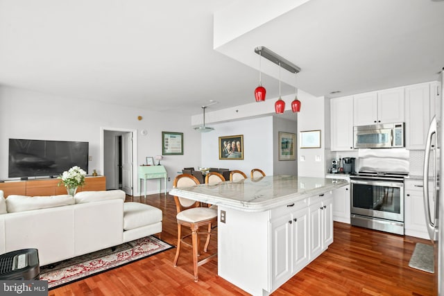 kitchen featuring a kitchen bar, stainless steel appliances, pendant lighting, white cabinetry, and a kitchen island