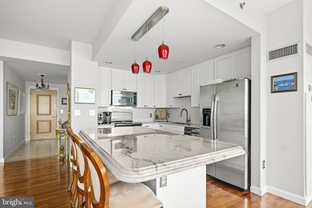 kitchen featuring white cabinets, decorative light fixtures, light stone countertops, and stainless steel appliances