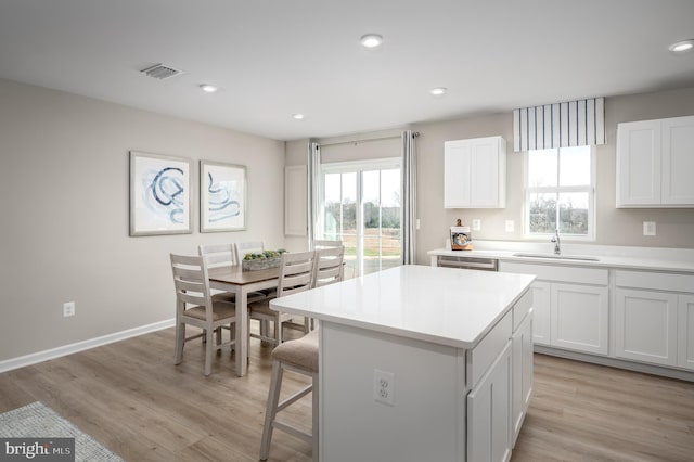 kitchen with sink, white cabinets, light wood-type flooring, and a kitchen island