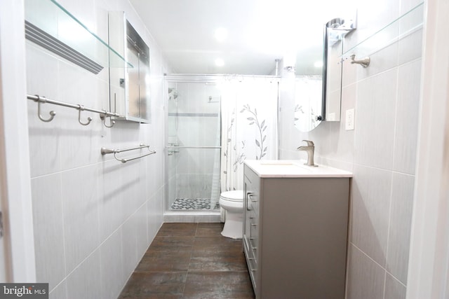 bathroom featuring vanity, toilet, a shower with door, and tile walls