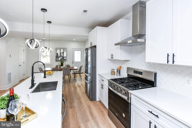 kitchen featuring white cabinets, stainless steel appliances, sink, wall chimney range hood, and decorative light fixtures