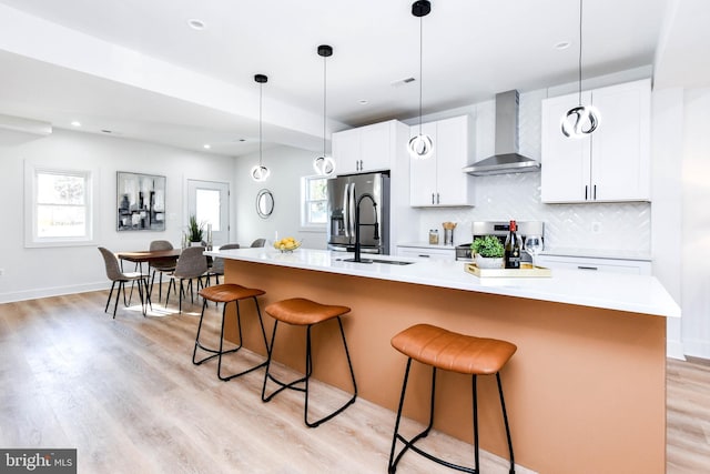 kitchen with stainless steel fridge, wall chimney range hood, stove, and a center island with sink