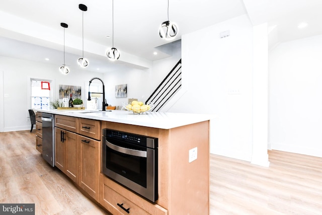 kitchen featuring sink, oven, light hardwood / wood-style floors, pendant lighting, and a kitchen island with sink