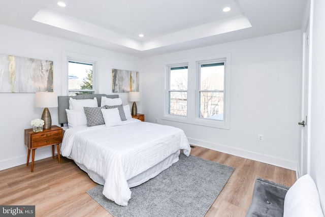 bedroom with a tray ceiling, light hardwood / wood-style flooring, and multiple windows