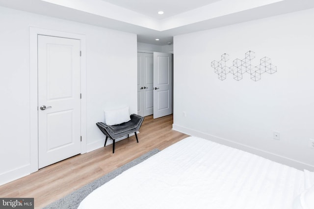 bedroom with light wood-type flooring and a tray ceiling